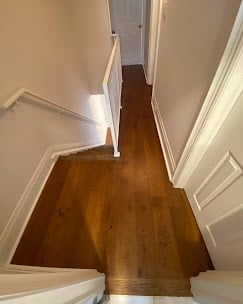 Wooden hallway with white trim and walls, viewed from above looking down a narrow corridor