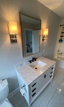 Modern bathroom with white vanity, marble countertop, rectangular mirror, and two brass wall sconces