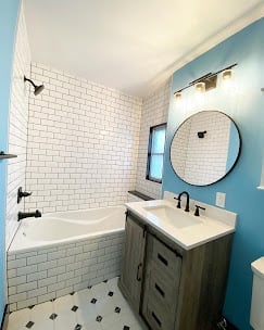 Modern bathroom with white subway tile shower, blue accent wall, round mirror, and wooden vanity with white sink