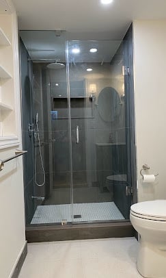 Modern bathroom with frameless glass shower enclosure, white tile floor, and toilet visible on the right side