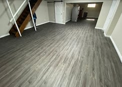 Empty room with gray wood-look vinyl flooring and white walls with doorways and construction materials