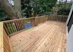 Newly constructed wooden deck with railings attached to a house, surrounded by green trees and vegetation