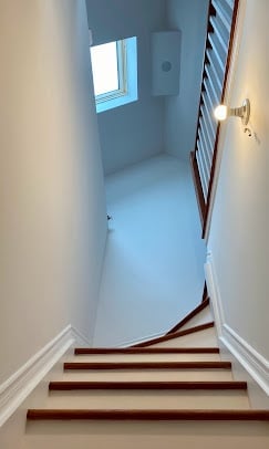 Stairway with wooden steps leading up to a bright room with a skylight window and a white towel rack on the right wall
