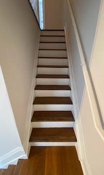 Wooden staircase with white walls viewed from bottom looking upward, showing steps leading to upper level