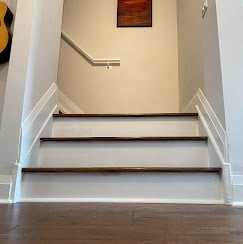 Staircase with wooden steps and white railings leading upward in a bright, well-lit interior hallway