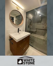 Modern bathroom with wooden vanity, white sink, round mirror, and frameless glass shower enclosure