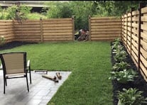 Backyard patio with green lawn, concrete patio, lounge chair, and wooden fence enclosure