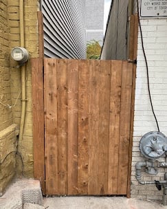 Wooden gate leaning against brick wall in narrow alleyway between buildings